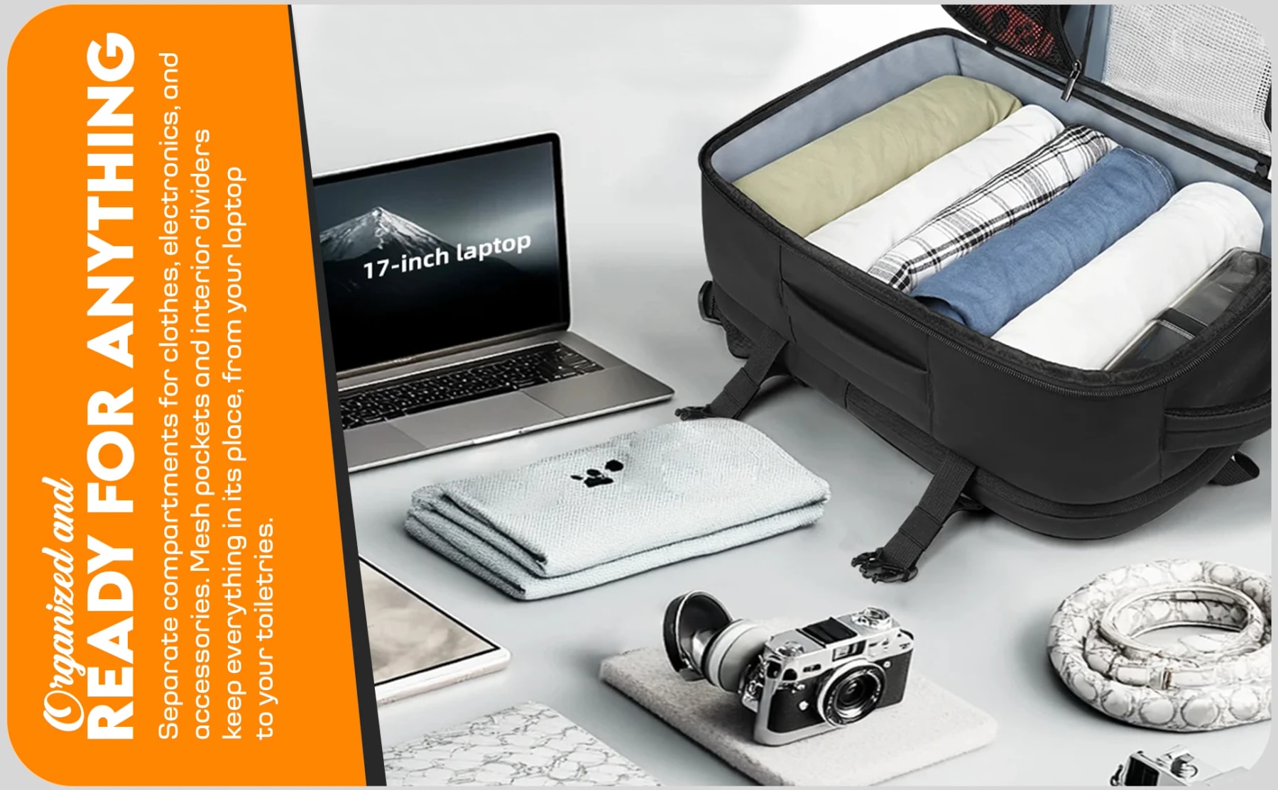 Open black travel backpack packed with rolled clothes beside a 17-inch laptop, camera and travel accessories.